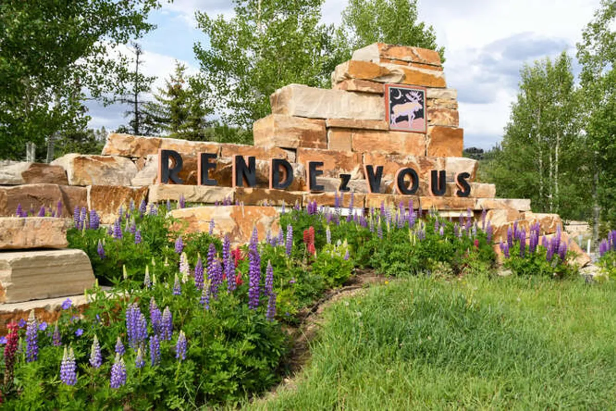 A picturesque exterior shot featuring a stone monument surrounded by colorful flowers and clear signage. The inviting landscaping suggests opportunities for exploration and moments of relaxation in a natural setting, capturing the essence of community and outdoor enjoyment.