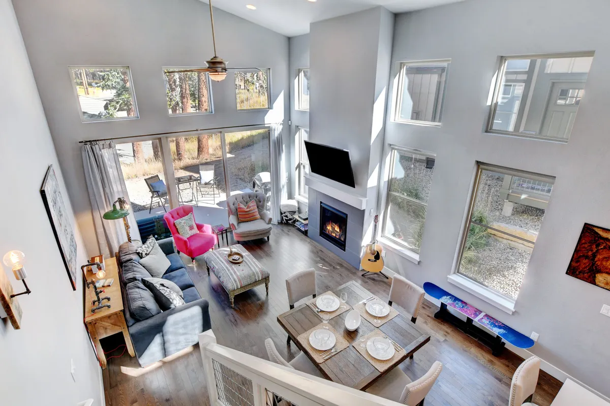 A bright, airy interior with large windows that showcase mountain views, a cozy fireplace, a dining table, and colorful chairs. The layout is ideal for relaxing or hosting gatherings, while the view outside connects the interior to the surrounding scenery.