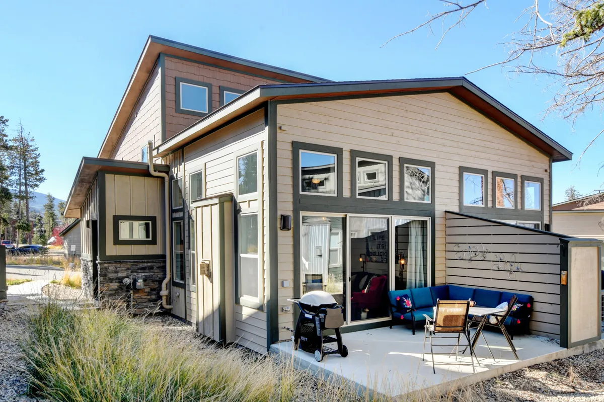 An inviting exterior patio scene featuring a large window backdrop, comfortable outdoor seating, and a grill. The area is staged for outdoor dining and social gatherings, with a view that hints at scenic surroundings and the welcoming ambiance of the patio space.