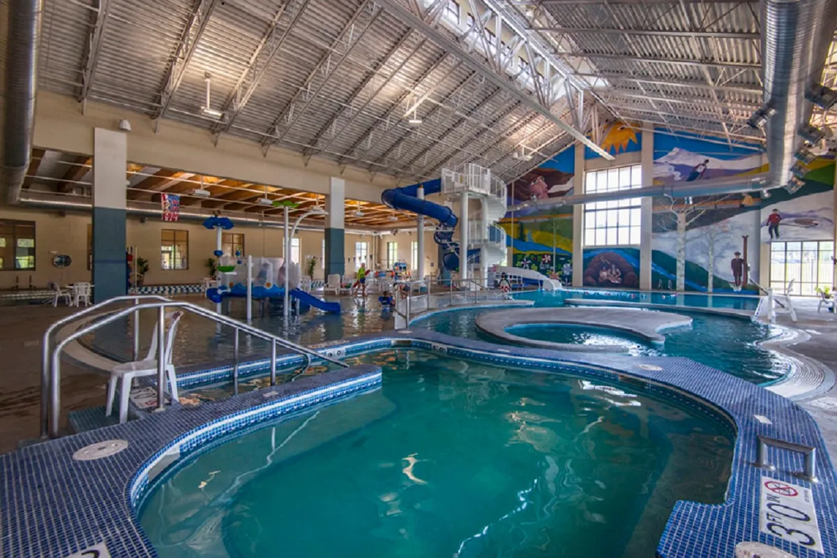 An inviting indoor pool area featuring colorful water slides and a playful atmosphere, perfect for kids and families. The mural and bright environment emphasize fun and active recreation even when the weather drives activities indoors.