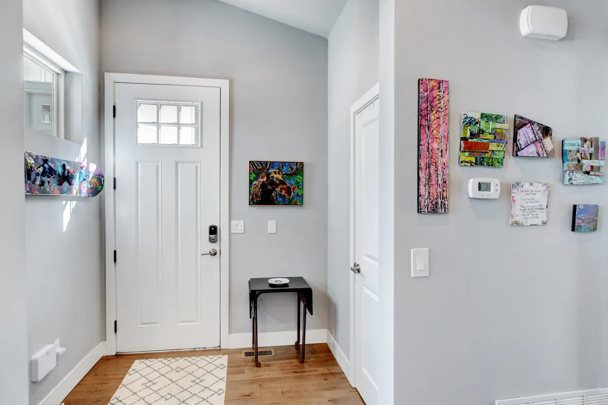 The inviting entryway features the front door, artistic wall decor, and a small table, creating a warm, welcoming atmosphere. The space is bright and creative, hinting at memorable arrivals and departures.