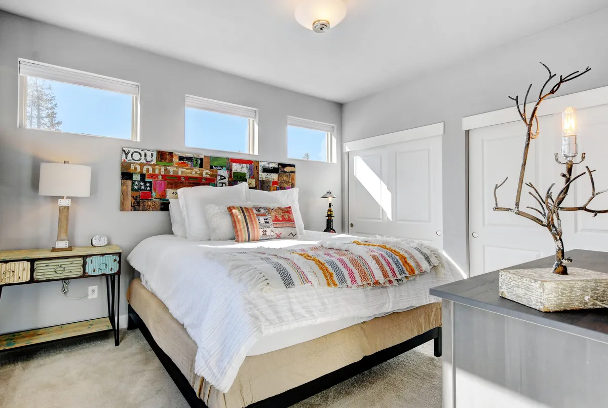 A tranquil bedroom featuring a cozy bed adorned with a decorative throw and plush pillows, complemented by calming wall art above the headboard. Soft natural light filters in, and bedside lamps provide a gentle ambiance, while a unique branch lamp adds a touch of character to the dresser.