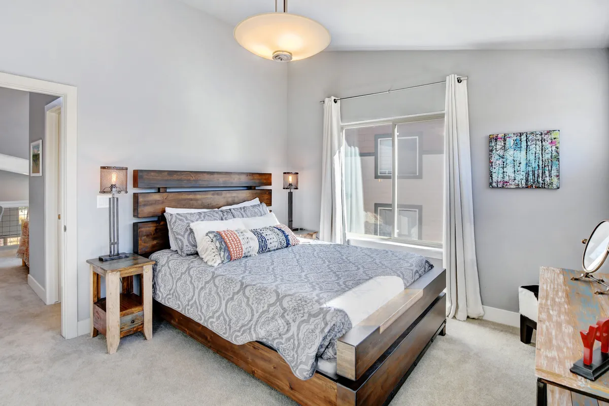 A serene bedroom scene with a bed dressed in patterned bedding, wooden bedside tables, large window streaming in natural light, and creative artwork on the wall. The space feels inviting and perfect for both relaxation and rejuvenation.
