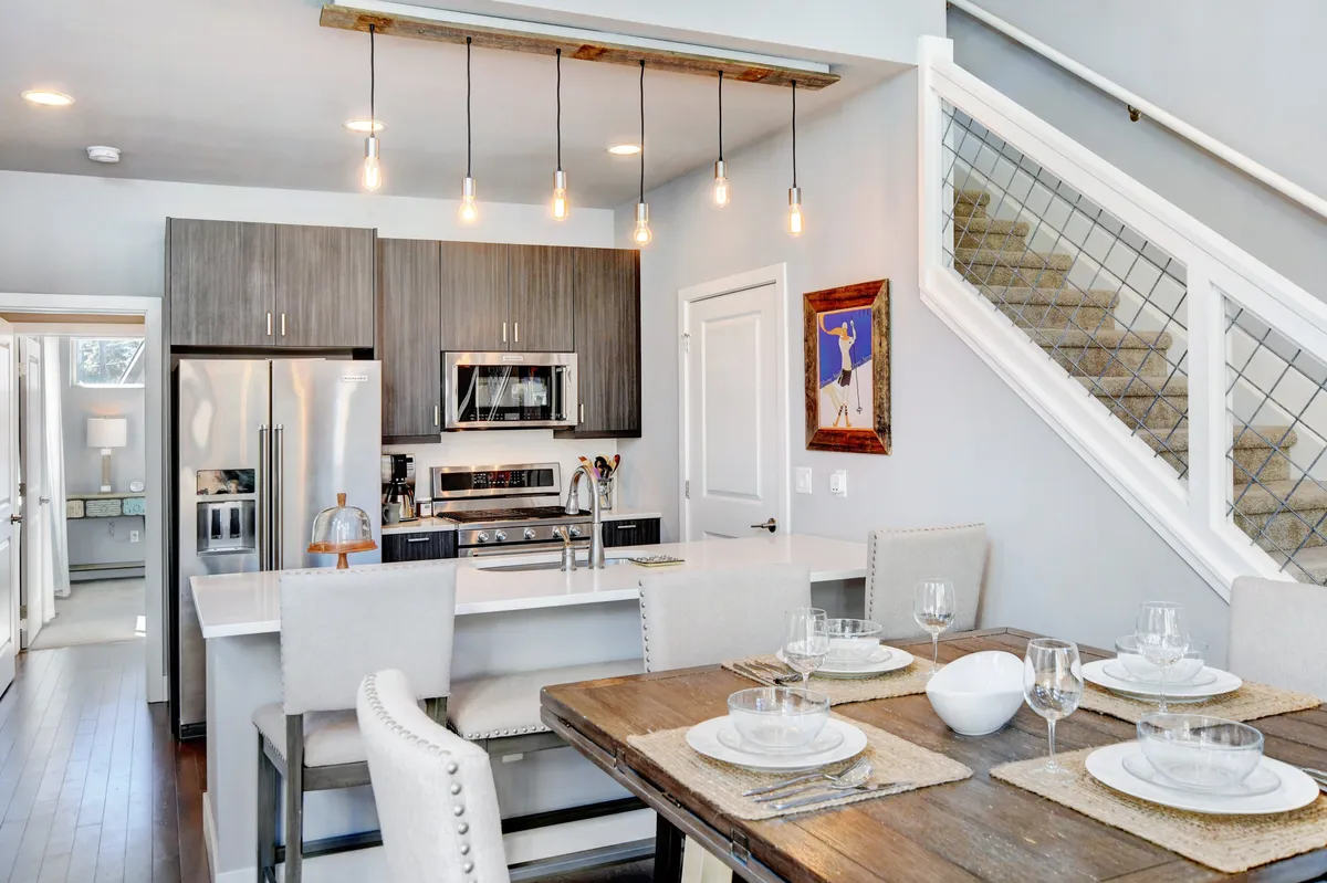 A spacious, modern kitchen with a central island, stainless steel appliances, custom tiled backsplash, and a dining table nearby. The setting is warm and welcoming, with artwork on the wall adding a homey touch. The open layout is ideal for both cooking and socializing, with space for entertaining guests or intimate dining.